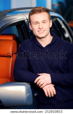 Happy car owner. Portrait of a handsome smiling man standing by his luxury car in the garage