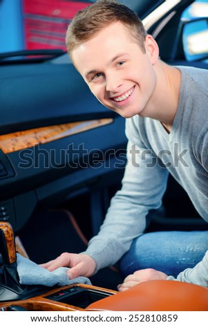 Cleaning his car. Closeup of handsome smiling young man cleaning his luxury car dash board and gear shift with a wiper