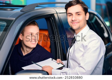 Best car rental. Handsome young car rental manager giving a copy space documents on clipboard to smiling client sitting a new luxury car