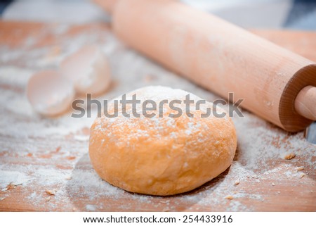 Rolling out the dough. Closeup of a raw dough and rolling pin placed on the wooden cutting board with dusting of flour in the kitchen