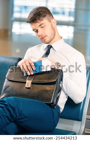Tired after a long business trip. Exhausted business man in formalwear sleeping while sitting on the rows of chairs in the airport holding his business case and passport