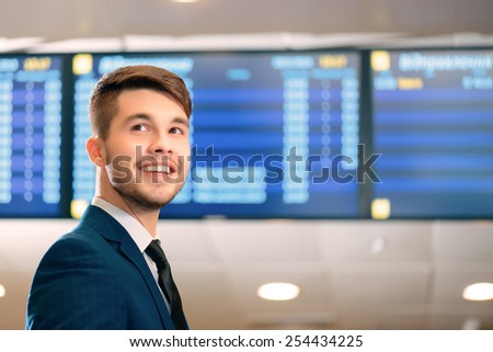 Just in time for check-in. Low angle image of a handsome businessman wearing  suit smiling away while standing against flights schedule in the airport