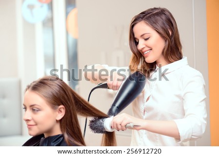 Stylish by professionals you can trust.  Mirror reflection of a young beautiful hairdresser doing her clients hair with a hair drier on the background of the hairdressing salon