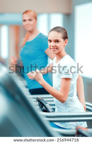 Cardio training. Side view of beautiful mature woman and her daughter in sports clothing having a workout on a treadmill in the gym