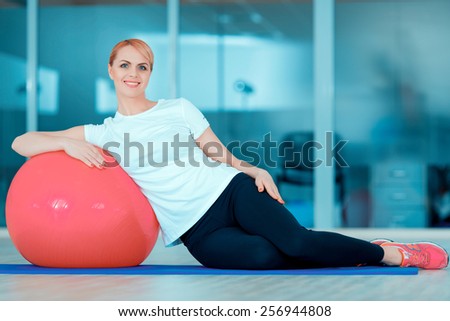 Fit and healthy. Portrait of attractive mature woman lying on fitness ball and smiling at camera while training in sports club
