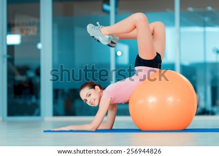 Happy to be fit. Portrait of attractive teenage girl lying on fitness ball and smiling at camera while training in sports club