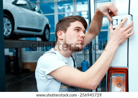 Double- check the door. Portrait of a concentrated handsome mechanic in uniform checking the door of the car at auto service station