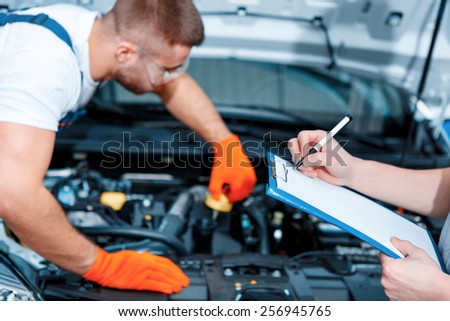Running diagnostics. Two handsome car mechanics in uniform checking the engine under hood in the car service station and checking in service order