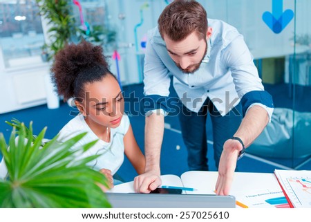 Creative team at work. Young African woman and Caucasian man in smart casual looking at laptop together while sitting in creative space