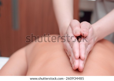 No stress. Beautiful young woman lying on front and keeping eyes closed while massage therapist massaging her back in spa