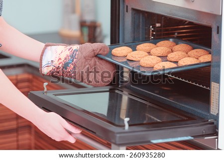 Baking day. Young beautiful woman putting a tray of home pastry in the oven