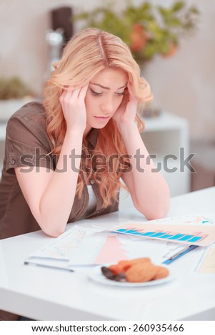 She needs help. Frustrated young woman in casual wear working with charts and analytics and touching her temples with fingers trying to understand