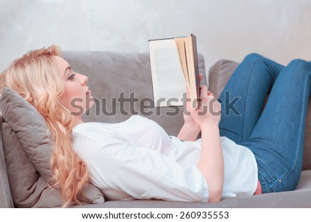 Reading her favorite book. Side view of confident female student reading a book while lying on the couch