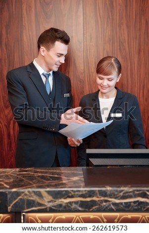 Reception at work. Male receptionist shows business papers to the female receptionist to discuss operating activity