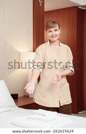 Perfect order. Maid in beige uniform points to the perfectly set towels on the hotel bed