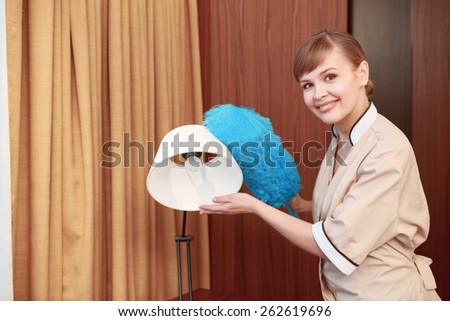 Only perfectly clean. Hotel maid paying attention to details as she uses a feather duster to dust off a lamp
