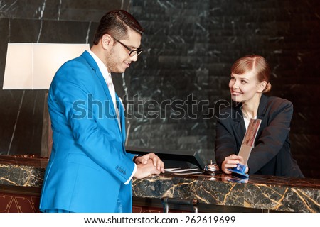 Do you have a spa. Good-looking businessman leaning against the hotel counter and viewing information holder which is displayed by a smiling female receptionist