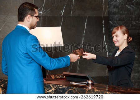 Check-in process. Selective focus of a handsome businessman in blue suit who passes his passport to a smiling receptionist behind the hotel counter