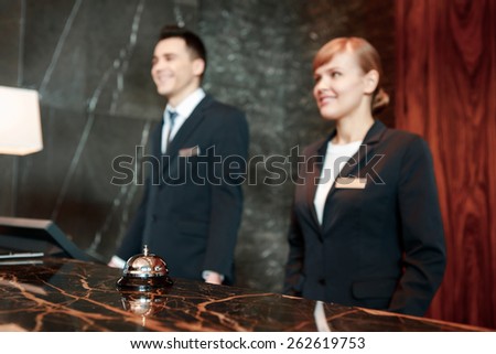 Can I help you. Selective focus on hotel service bell put with female and male receptionists in uniform standing behind the counter in blurry