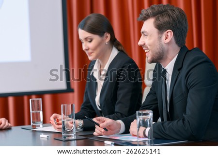 Feel at ease. Two business looking managers in black suits laugh sitting by the table in meeting room
