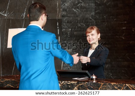 Welcome at our hotel. Selective focus of a beautiful female receptionist passing over a key to the guest who checks-in at a reception desk