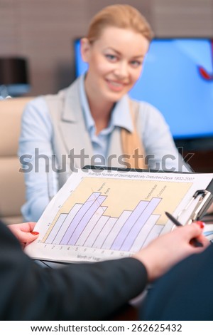 Look at the data. Closeup with the selective focus on the clipboard with business data, attractive blonde female business manager on the background