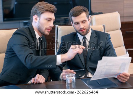 Smart solutions for business. Two good-looking managers in black suits looking at the business data and discussing business trends