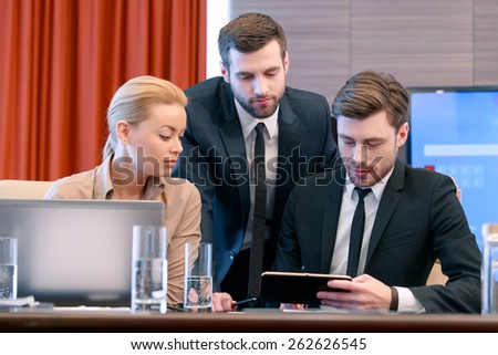 And this looks interesting. Two good-looking businessmen in formalwear and an attractive blonde female business partner looking and analyzing information on the tablet device
