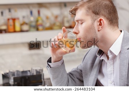 Friday night. Young man in shirt and jacket drinking whiskey with ice sitting at the bar counter