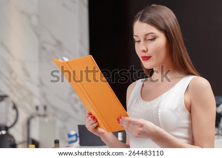Choice of the drink. Young attractive brunette looking through the menu while sitting at the counter of the bar