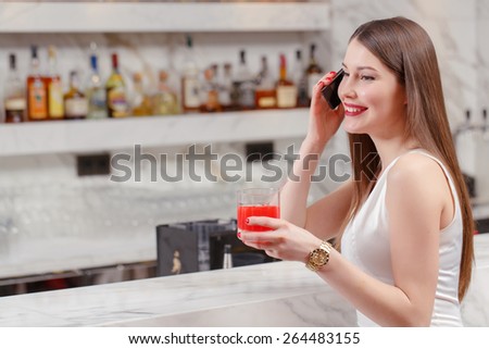 Friendly phone conversation. Attractive young woman talks over the phone while drinking a cocktail in the bar
