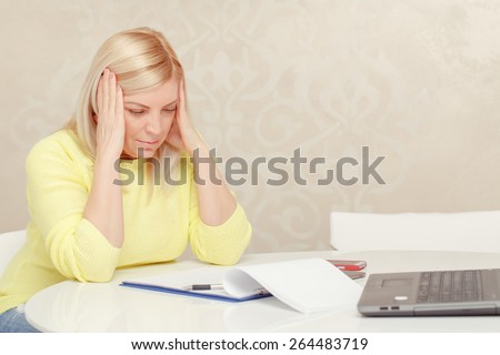 Hard decision making process. Attractive mature woman holding her head in hands thinking over the business papers on the table