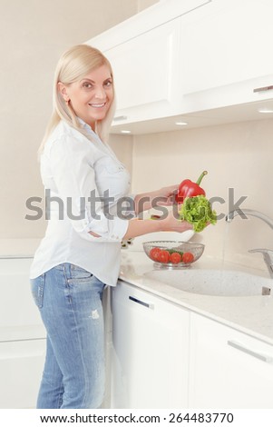 Woman cooking in the kitchen. Good-looking blond woman washing vegetables in a kitchen sink getting ready to cook salad for lunch