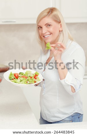 Healthy meals for any occasions. Smiling blonde woman holds a plate with fresh salad cooked in her home kitchen