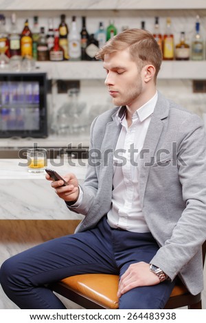 Anticipating a meeting. Young man in shirt and jacket talking over the phone and looking at his watch while sitting at the counter of the bar