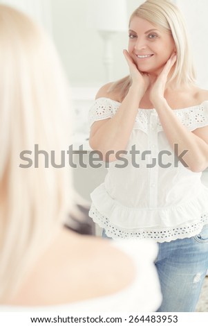 Never felt better. Beautiful middle aged woman looking at the mirror, smiling and touching her face
