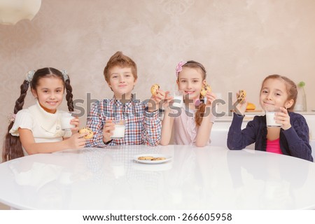 Tasty and healthy meal. Small school kids drinking milk with biscuits by the table at home and smiling at a camera