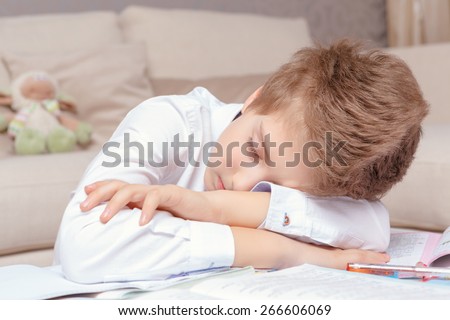 Sleepy science. Close-up of a small school boy laying his head on his hands fallen asleep while studying at home
