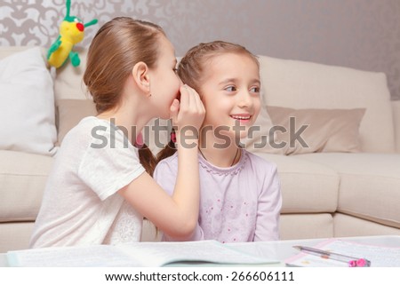 Girl gossiping. Cute schoolgirl having fun whispering something into the ears of her friend