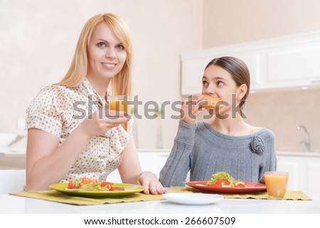 Healthy meals. Smiling mother and her pretty teen girl eating salad and drinking carrot juice by lunch at home