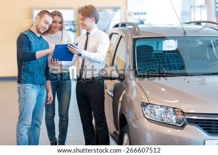 Just sign up the papers and the car is yours. Handsome young salesman holding a clipboard so that male customer could sign up the papers to buy a new car