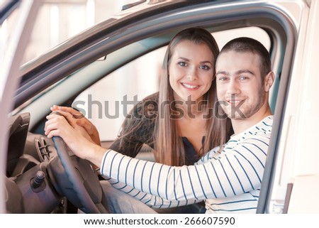Feel the drive. Young male customer with his attractive couple sitting inside the car by the steering wheel and examining interior of the car