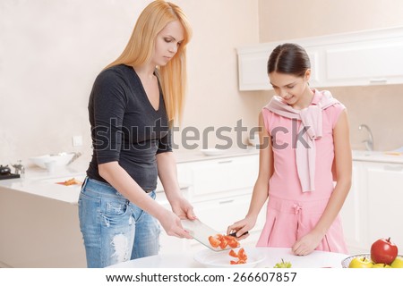 Cooking process. Beautiful mother showing to the daughter process of slicing tomatoes for fresh vegetable salad