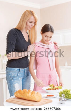 Keep fit. Beautiful mother and daughter looking at the dish with salad standing on a kitchen table