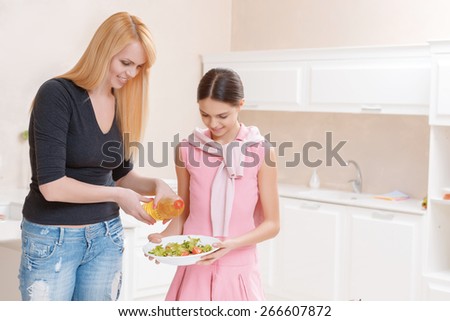 Salad dressing. Smiling mother and her tiny teenage daughter fill fresh salad with oil