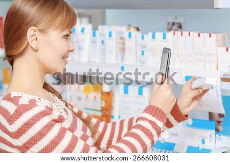 Buying medicine. Young smiling woman making photo on her phone of a medicine in a drugstore