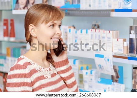 Family care. Young smiling customer of a drugstore speaks over the phone looking at the medicines on the shelves