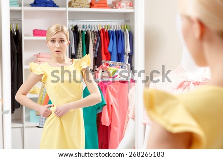 Too loose. Young girl looking with disappointment into the mirror fitting her dress on the belt