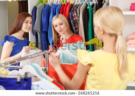 Shopping with friends. Selective focus on two female shoppers assessing choice of their friend standing in front of them with a hanger