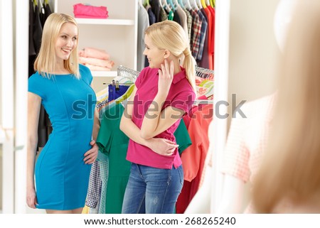 Perfect match. Shop assistant is talking to a smiling customer wearing a new blue dress